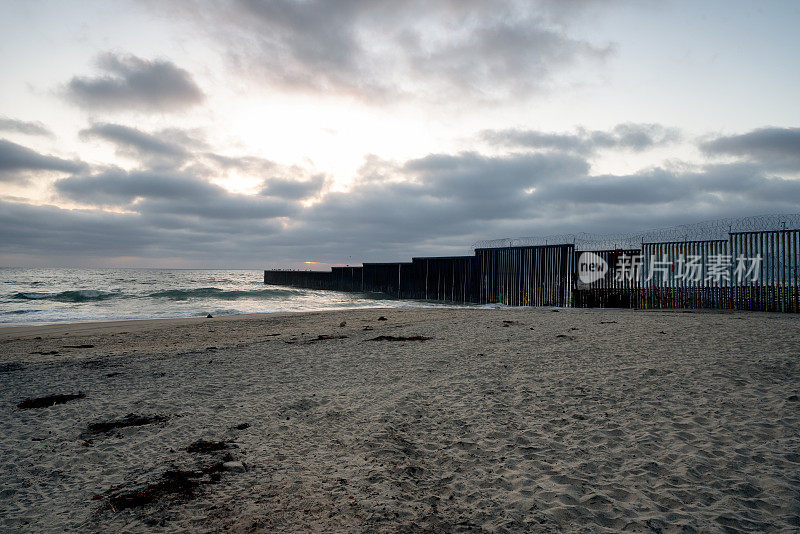 海滩和海浪的近景日落附近的国际边界墙在Playas Tijuana，墨西哥